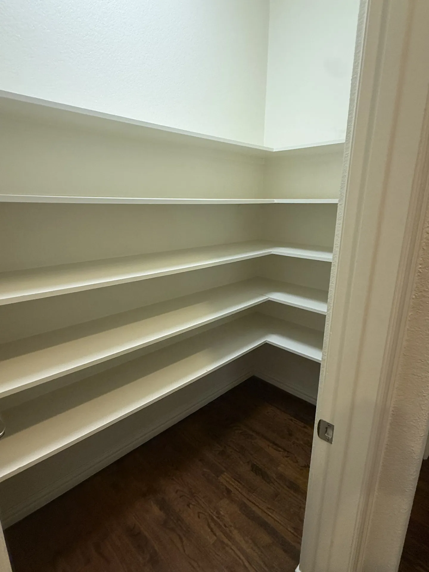 Corner pantry featuring multiple white shelves and wood-finish flooring