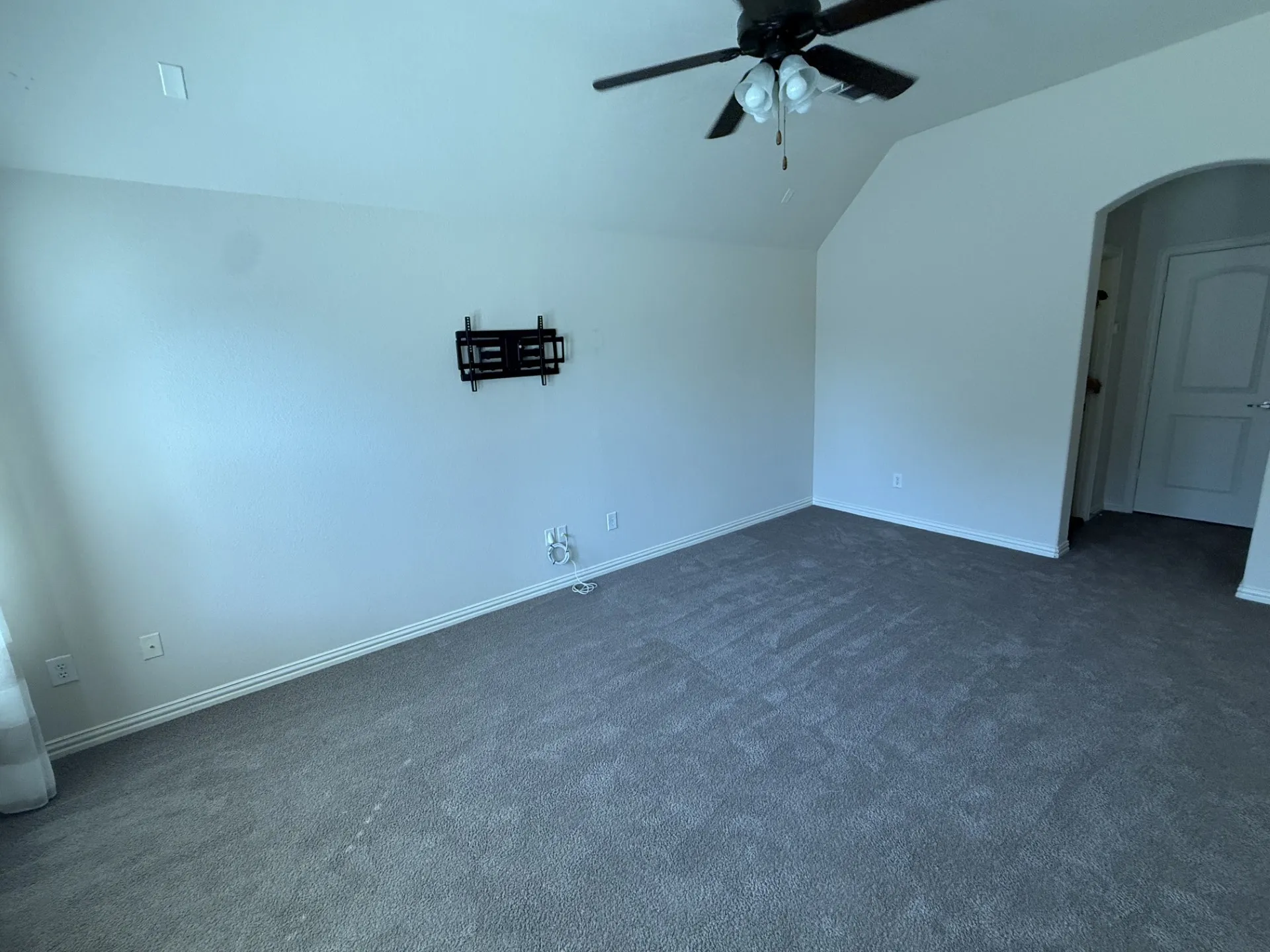 Carpeted room featuring a ceiling fan, sloped ceiling, and an arched doorway