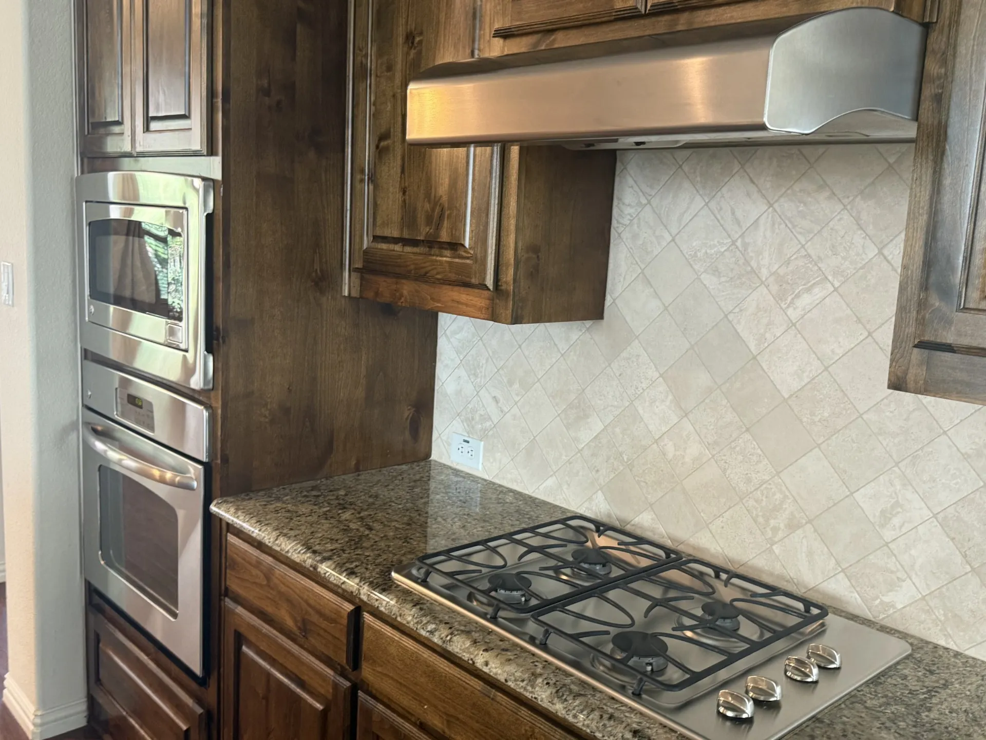 Stainless steel built-in microwave and oven, gas cooktop, granite-finish countertops, and wood-finish cabinetry