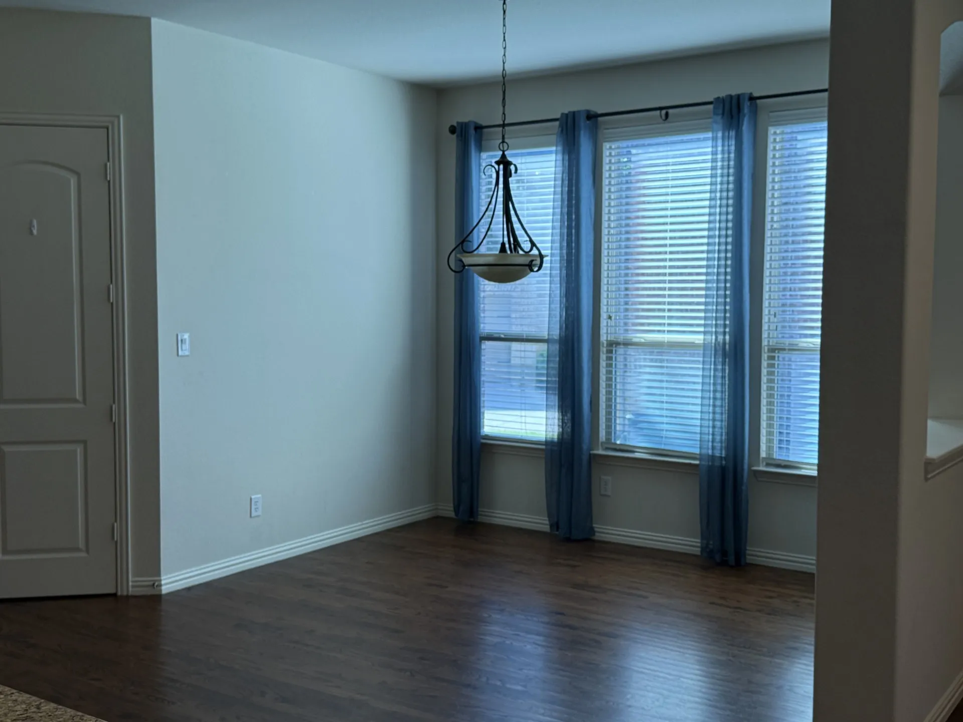 Hardwood-finish flooring, three large windows, and a hanging light fixture create an inviting atmosphere