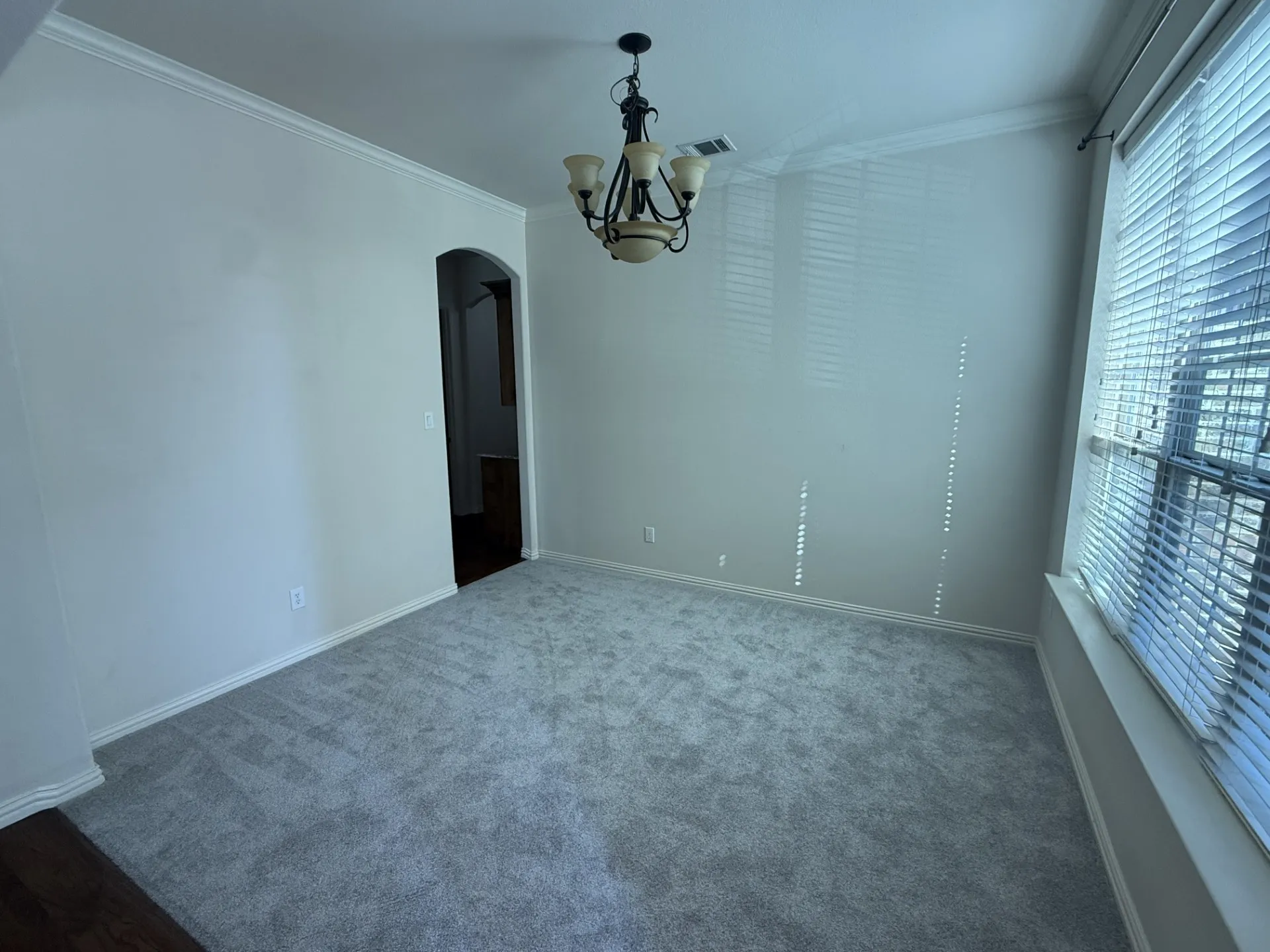 Recessed window with blinds, ceiling-mounted chandelier, light-toned wall paint, and gray carpet flooring
