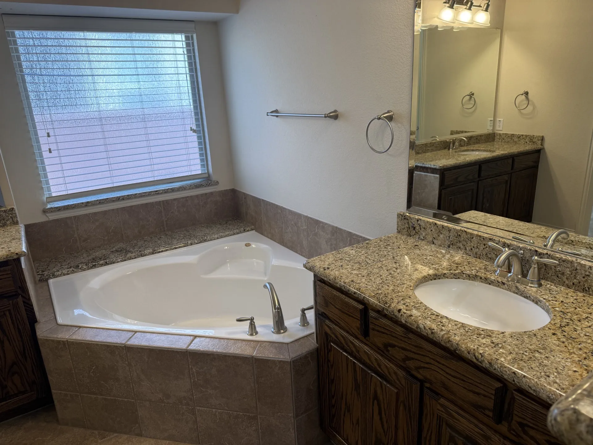 Deep soaking tub, dual vanity with undermount sinks, granite countertops, wood-finish cabinetry, and tiled tub surround