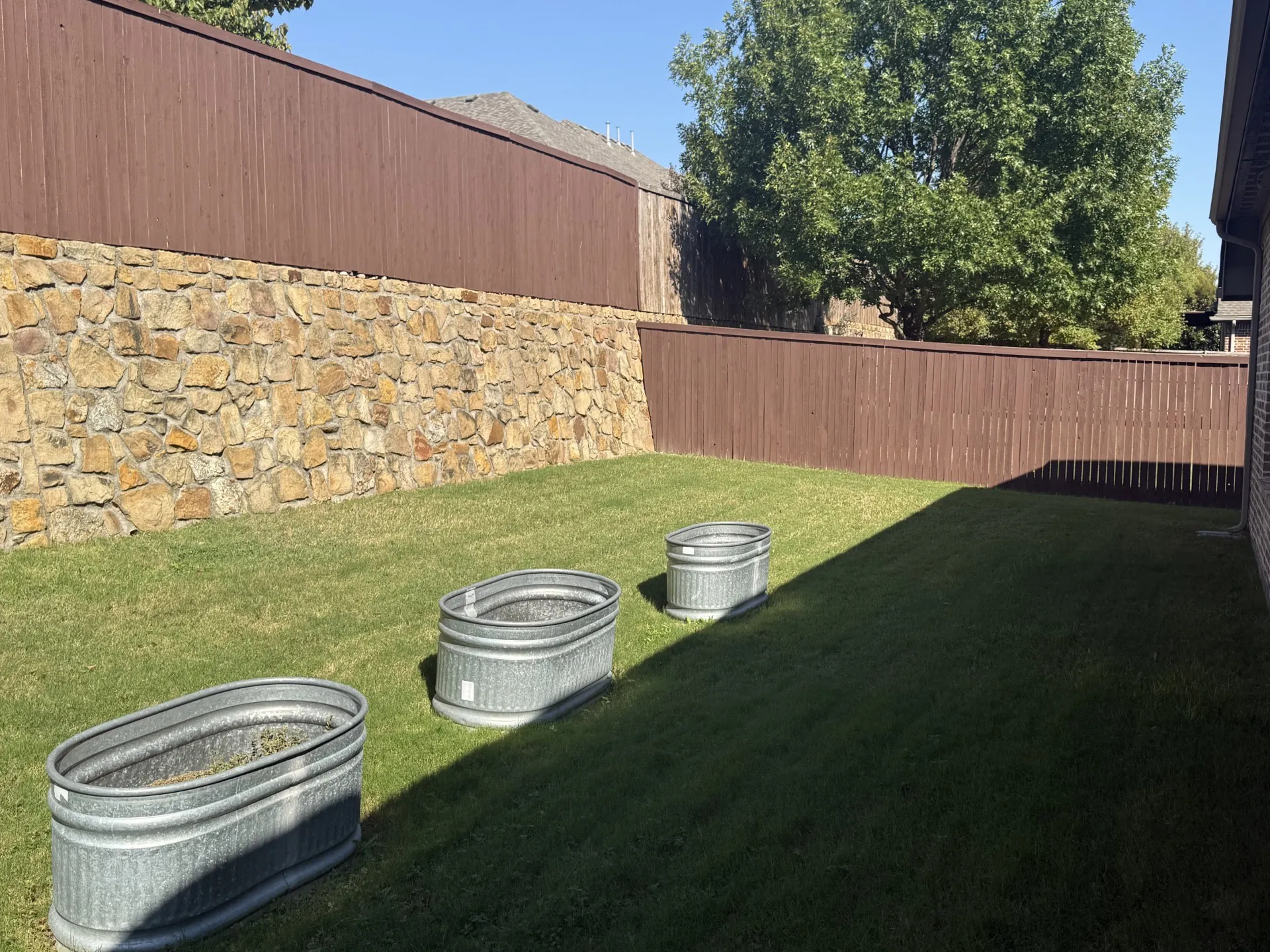 Expansive lawn area featuring a stone retaining wall and a wood privacy fence