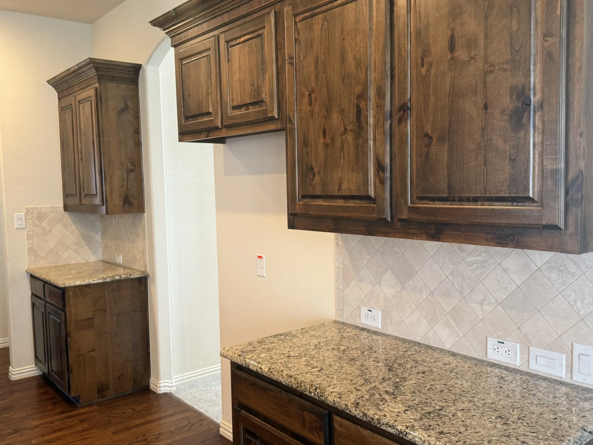 Wood-finish cabinetry with crown molding, stone countertops, and a tiled backsplash