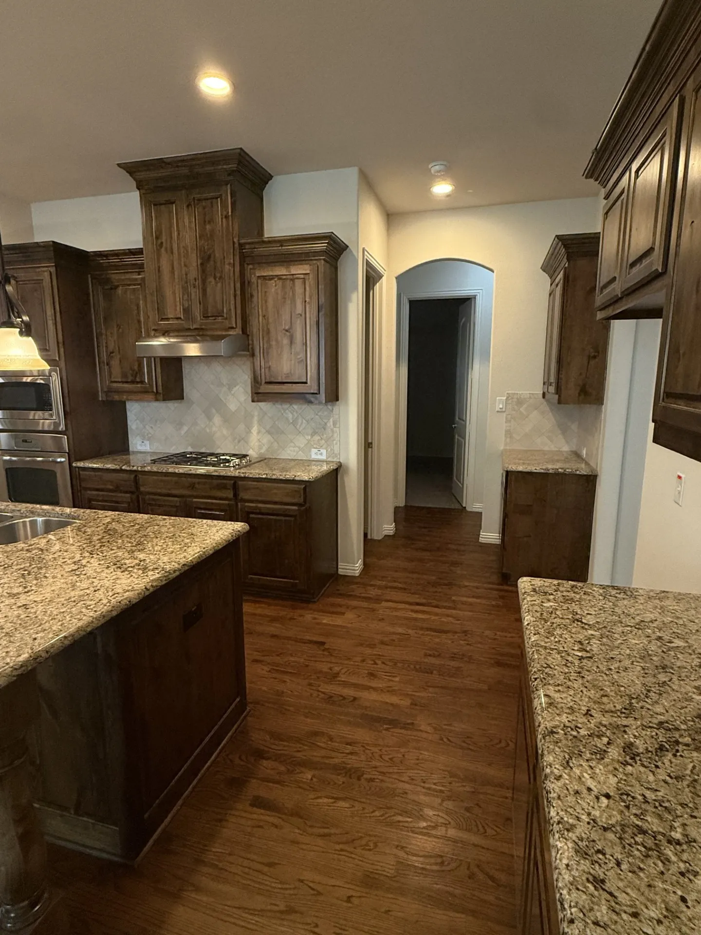 Wood-finish flooring, dark wood cabinetry, light-toned countertops, and a tile backsplash