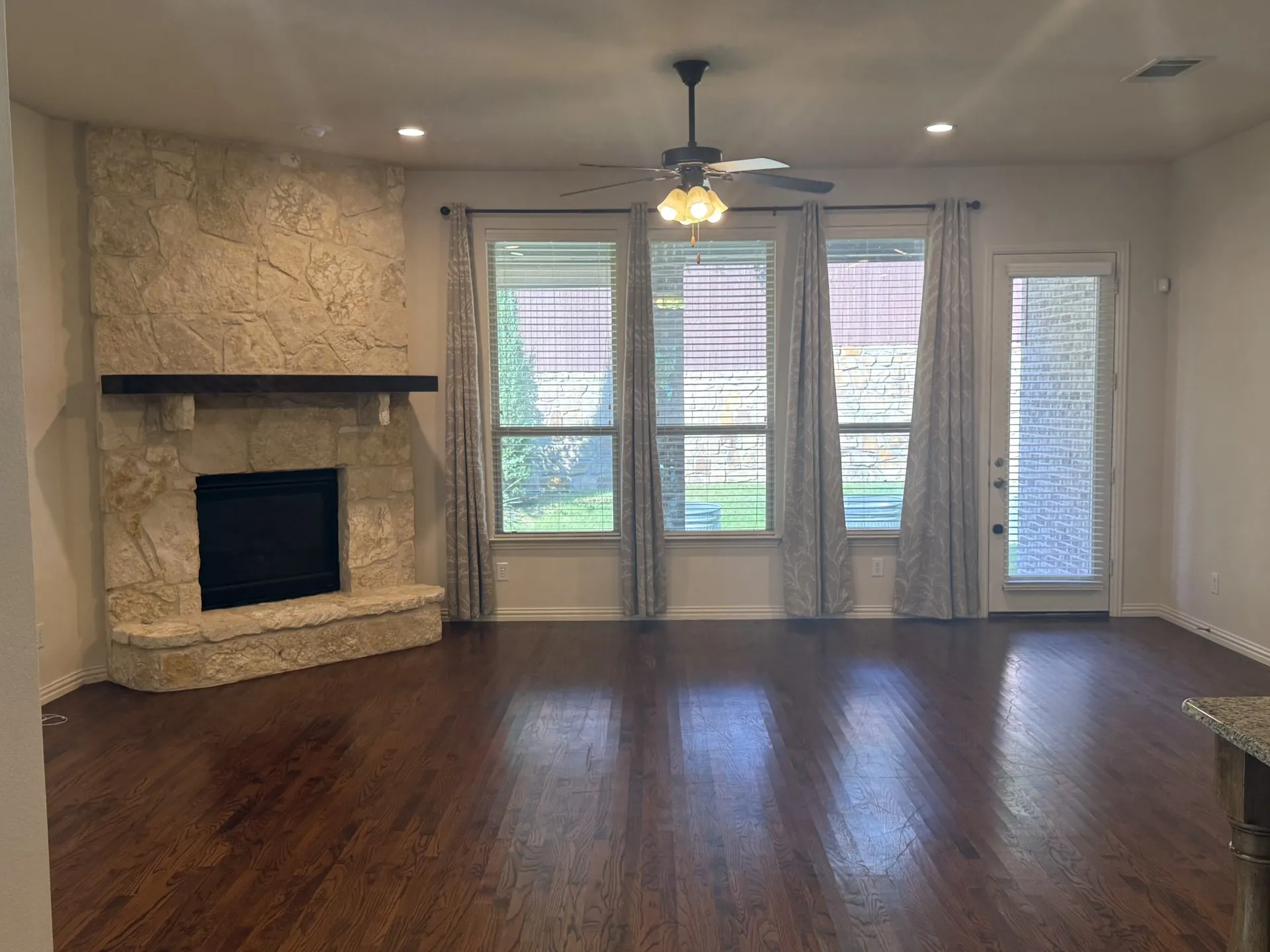 Stone-clad fireplace with a wood mantel, dark wood-finish flooring, recessed lighting, and a ceiling fan