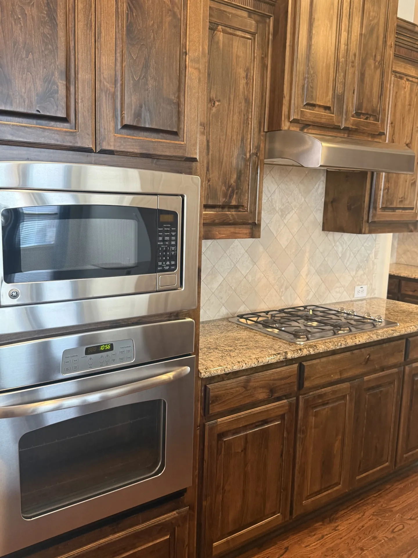 Built-in stainless steel microwave and oven, gas cooktop, granite countertops, wood cabinetry, and diamond-patterned tile backsplash