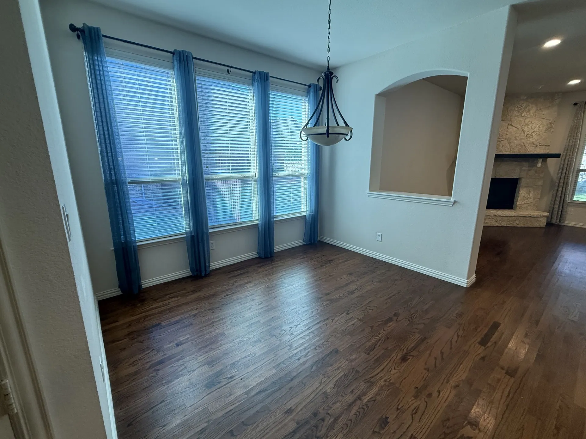Hardwood-finish flooring with a decorative chandelier, multiple windows with blinds, and an integrated wall niche