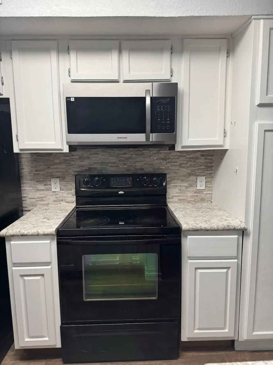 Kitchen with black range with electric cooktop, white cabinets, stainless steel microwave, and backsplash