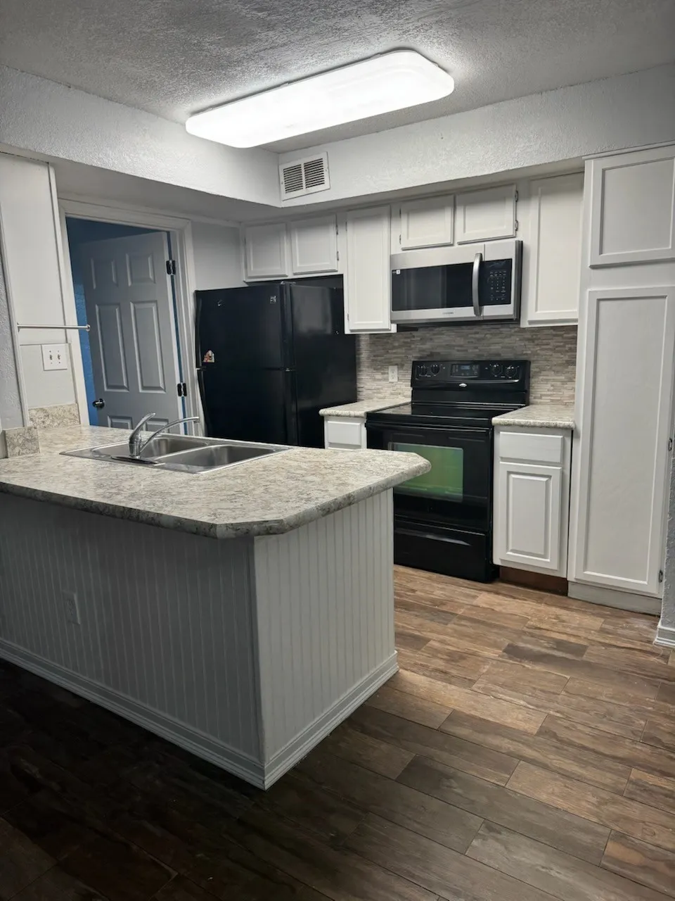 Kitchen with white cabinetry, black appliances, light countertops, dark wood-type flooring, and a peninsula