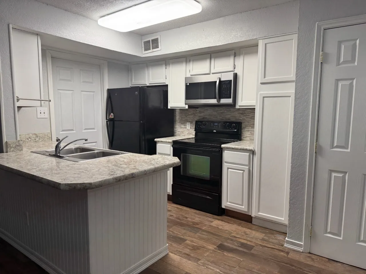 Kitchen with black appliances, light countertops, a textured wall, white cabinets, and a peninsula