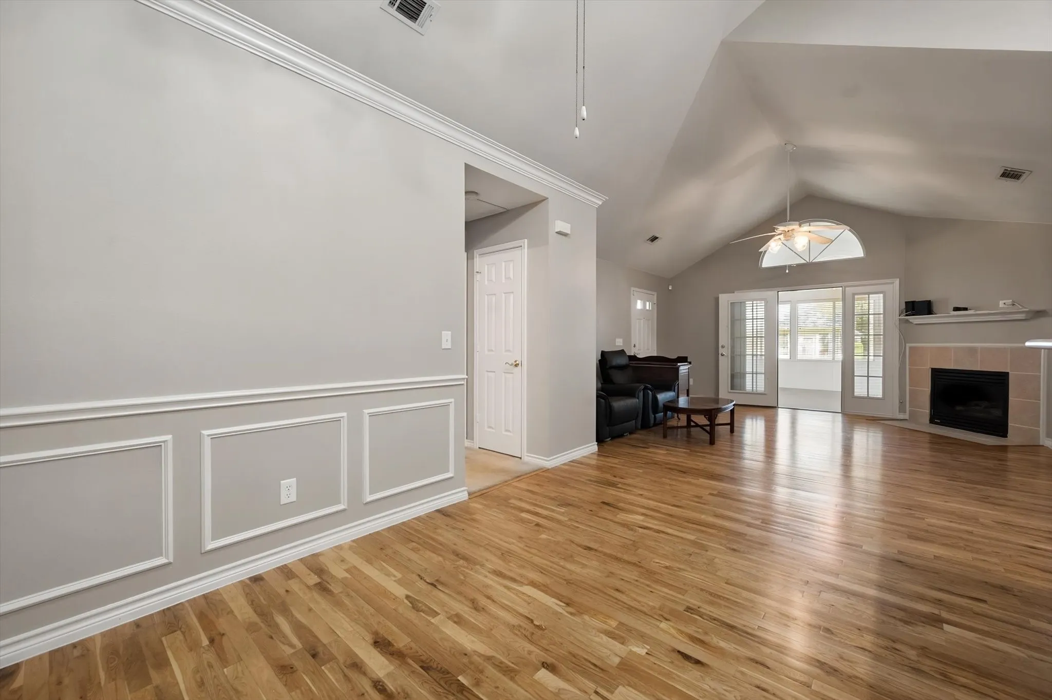 Vaulted ceiling, wood-finish flooring, wainscoting, sliding glass doors, and a tiled fireplace