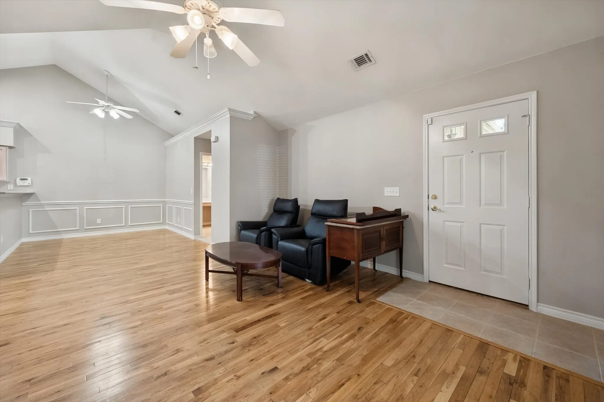 Vaulted ceiling with dual ceiling fans, wood-finish flooring, and wainscoting