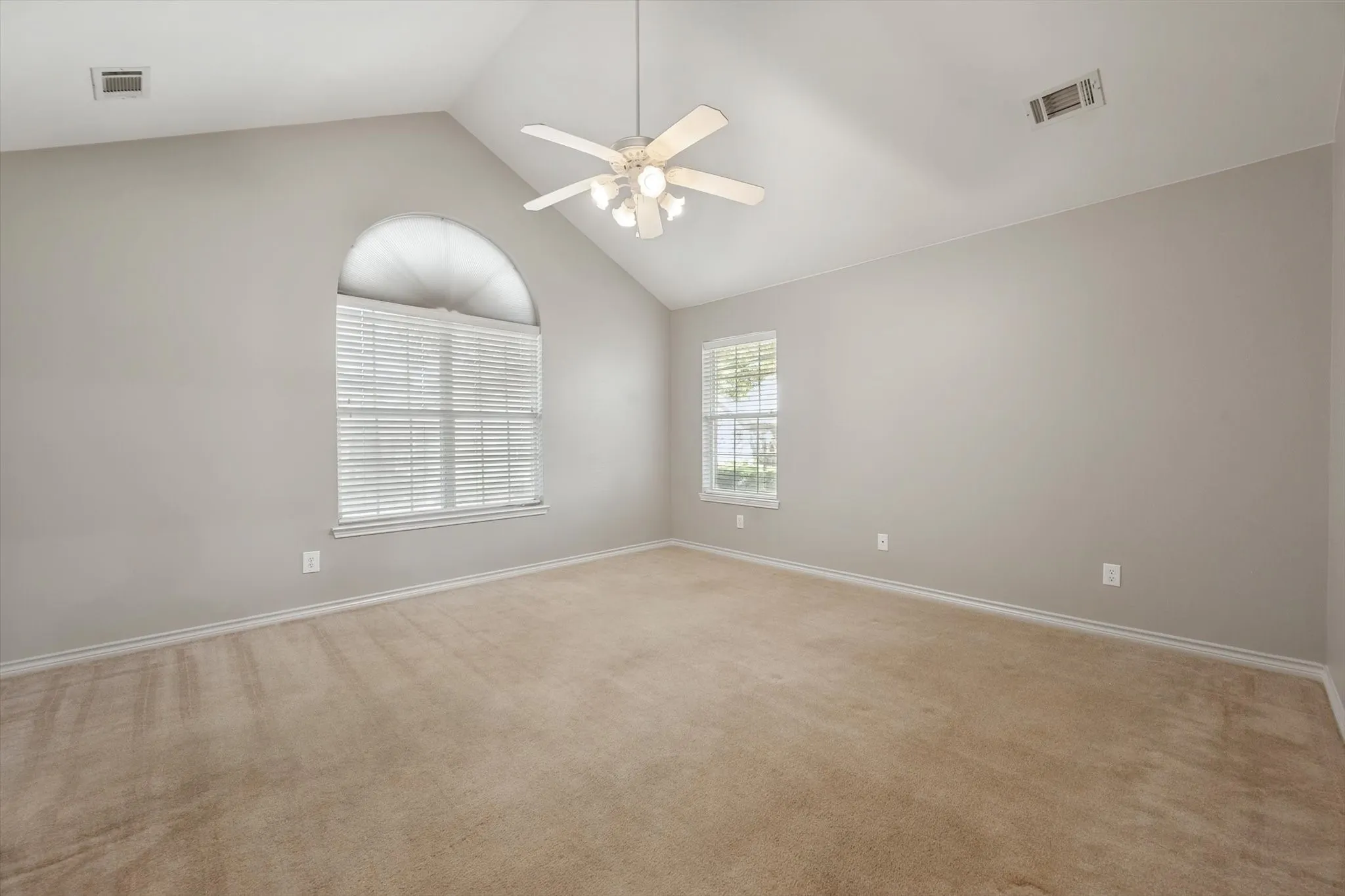 Vaulted ceiling, arched window with blinds, additional rectangular window, neutral-toned walls, and ceiling fan with integrated lighting