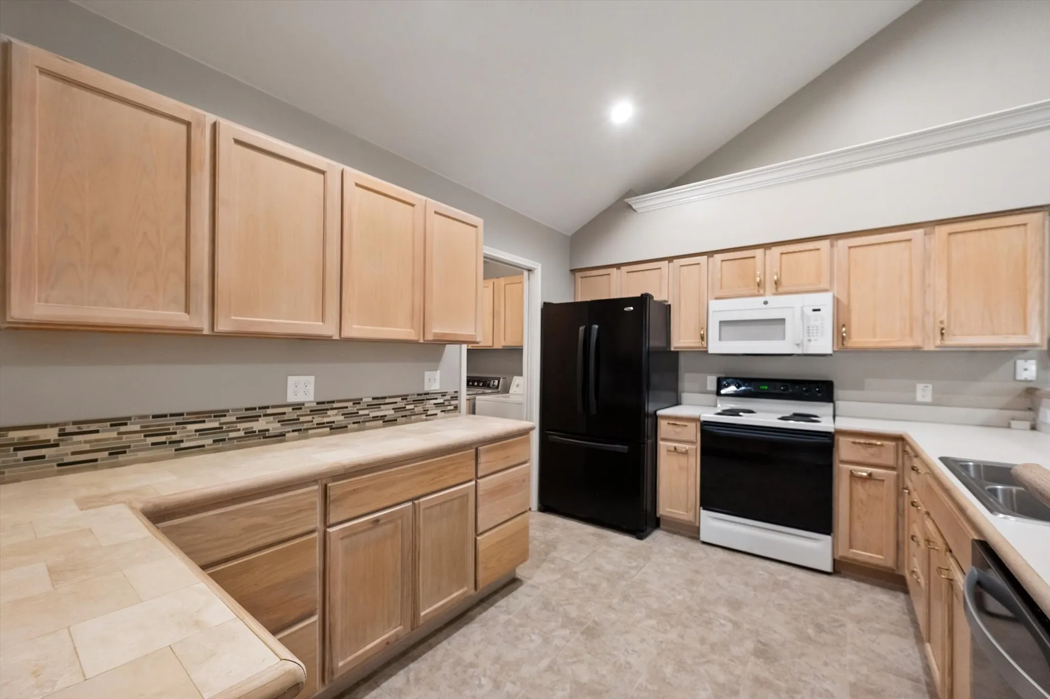Kitchen featuring wood-finish cabinetry, tile backsplash, built-in microwave, and vaulted ceilings