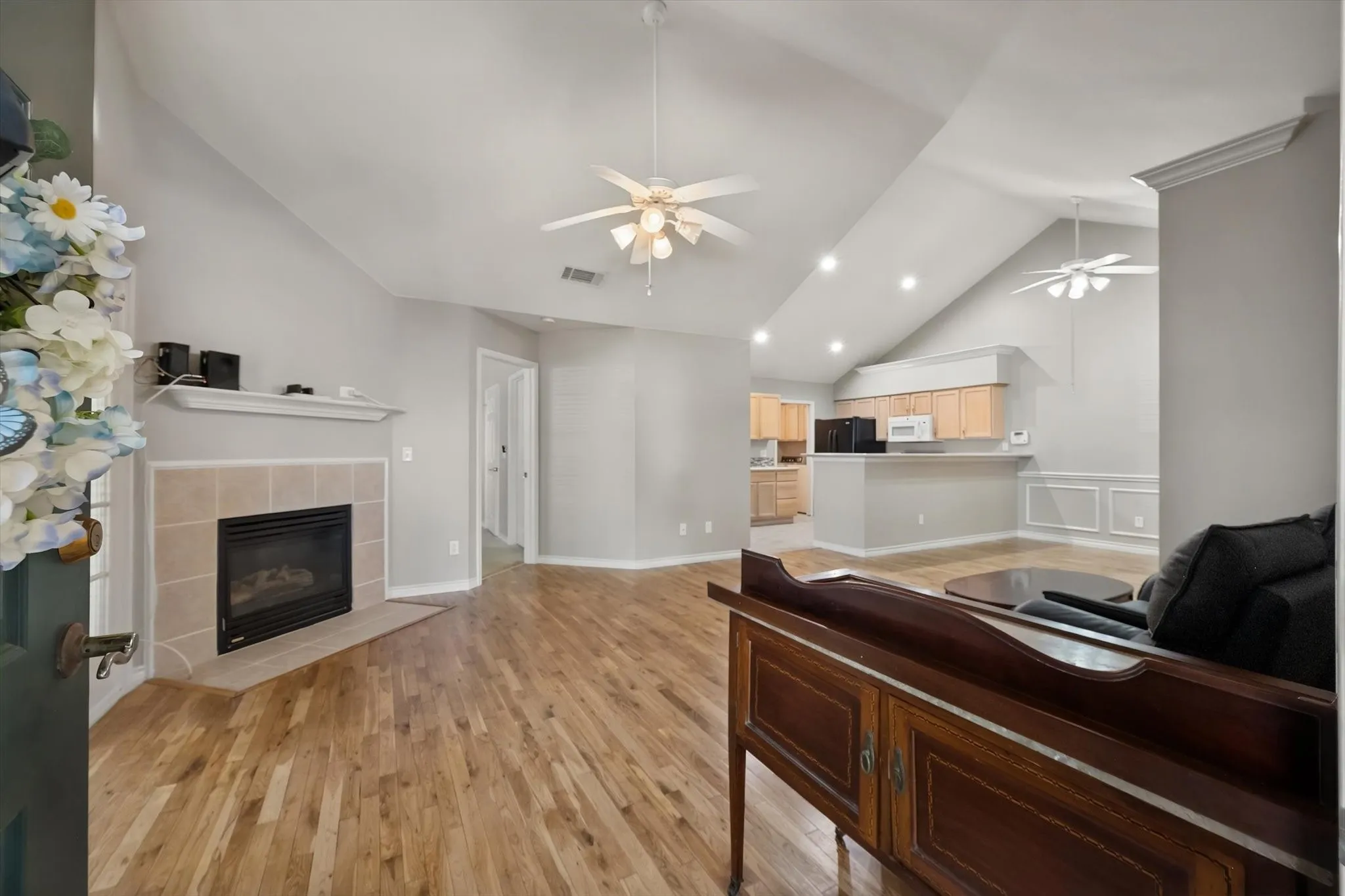 Vaulted ceilings with recessed lighting, wood-finish flooring, and a fireplace with a tile surround and mantel