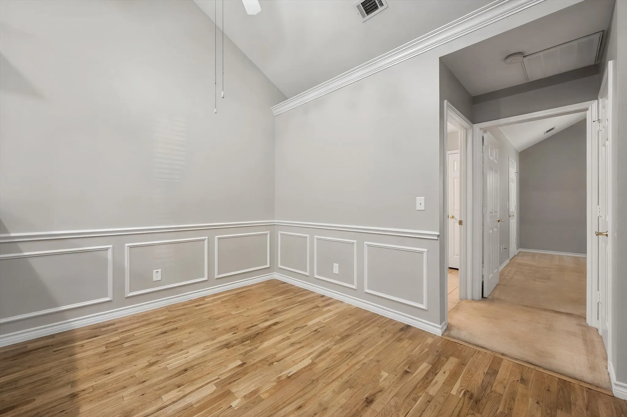 Vaulted ceiling, wood-finish flooring, decorative wall molding, and white trim