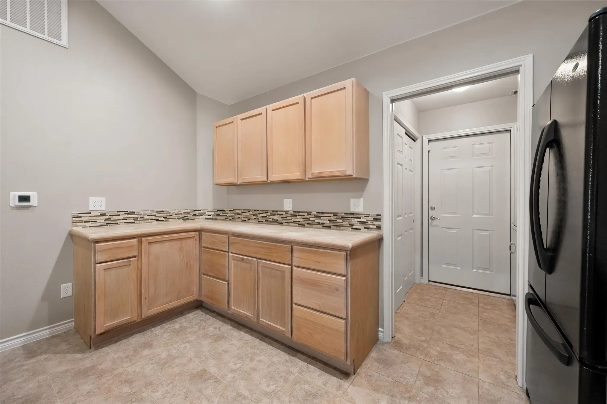 Light wood-tone cabinetry with an integrated countertop, mosaic tile backsplash, and tile flooring