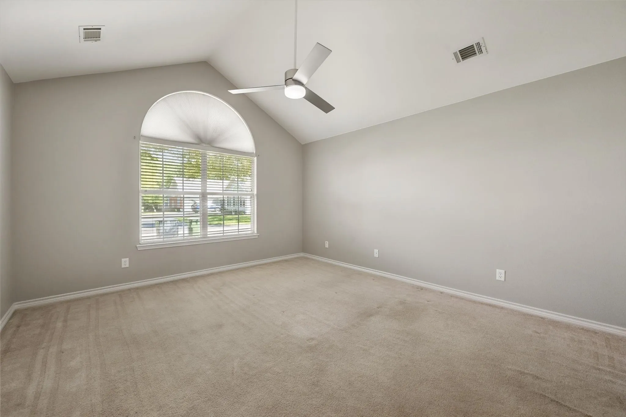 Vaulted ceiling, arched window with blinds, ceiling fan with integrated lighting, and neutral carpeting