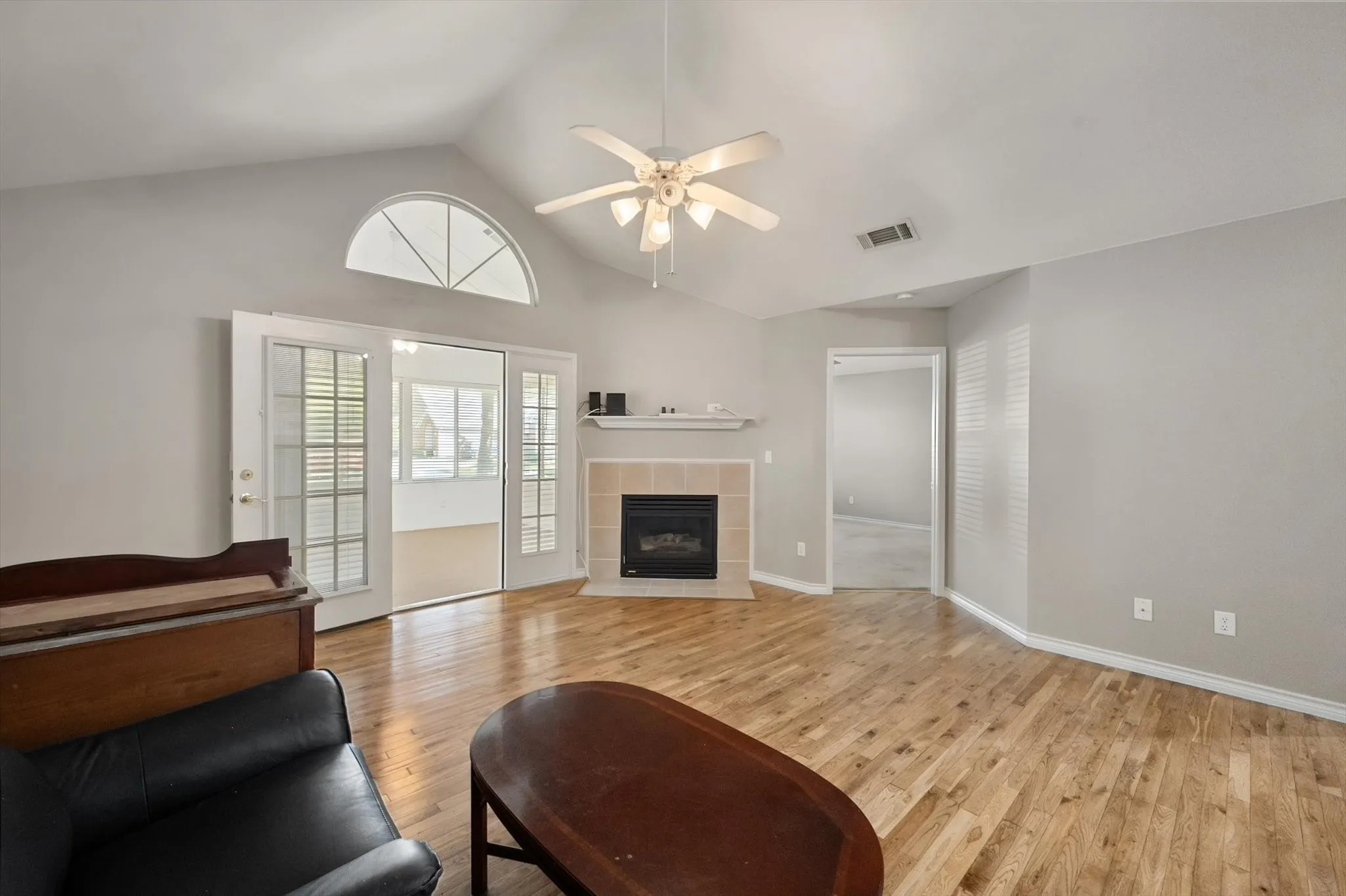Vaulted ceiling with ceiling fan, wood-finish flooring, corner fireplace with tile surround, and French doors