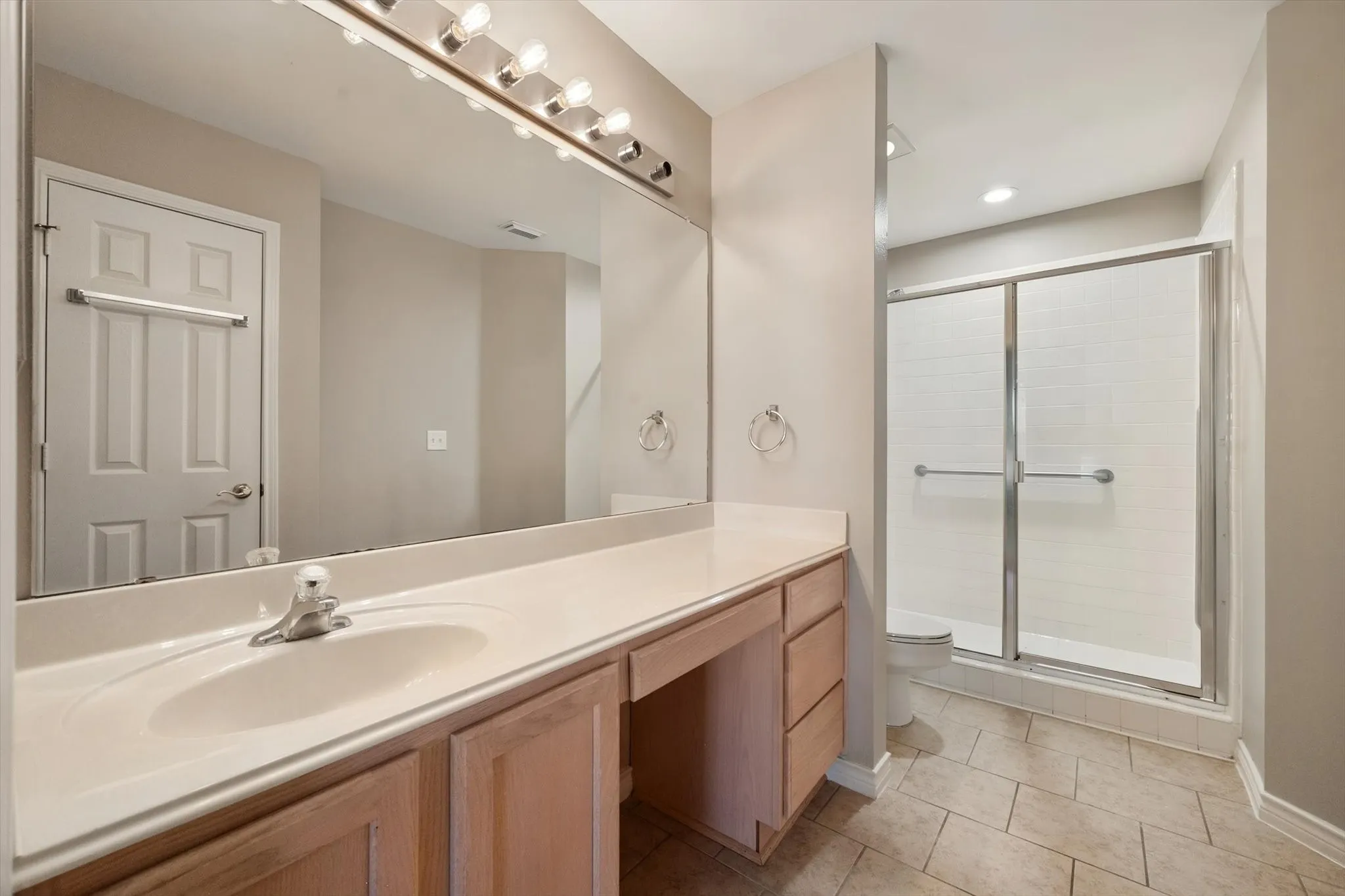 Spacious vanity with an integrated sink and light wood-finish cabinetry, illuminated by a strip light fixture