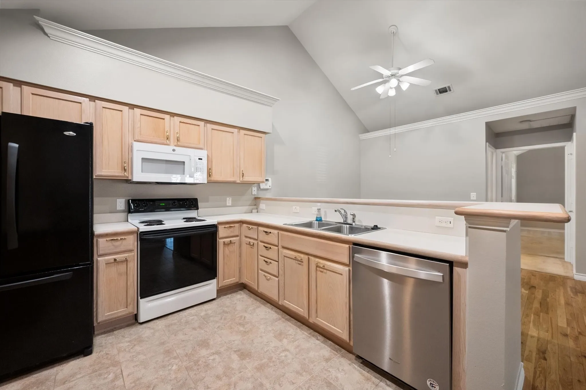 Kitchen featuring light wood-finish cabinetry, a built-in microwave, a stainless steel dishwasher, and a dual basin sink