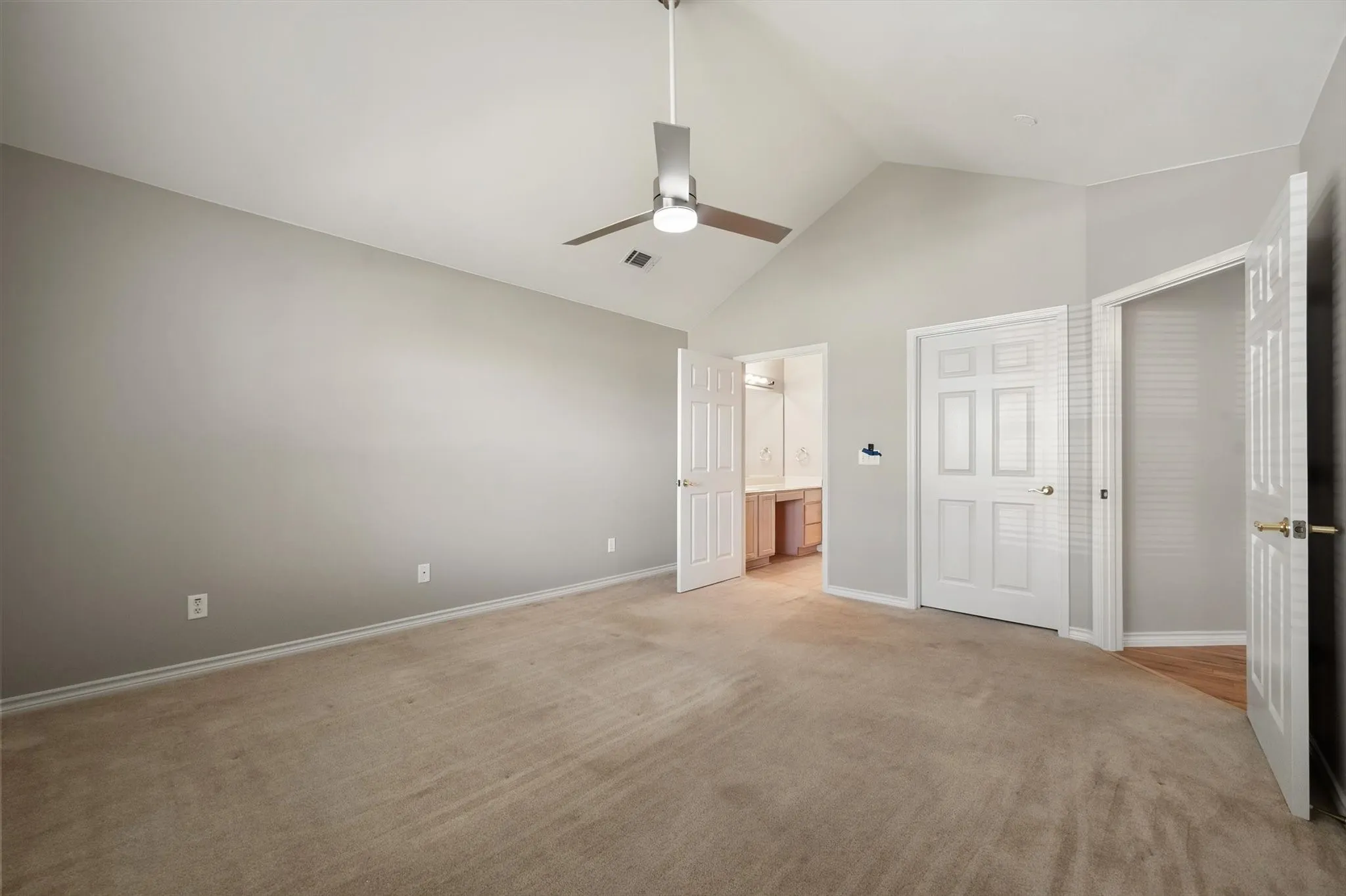 Vaulted ceiling, ceiling fan, neutral carpet, light gray wall color, white interior doors