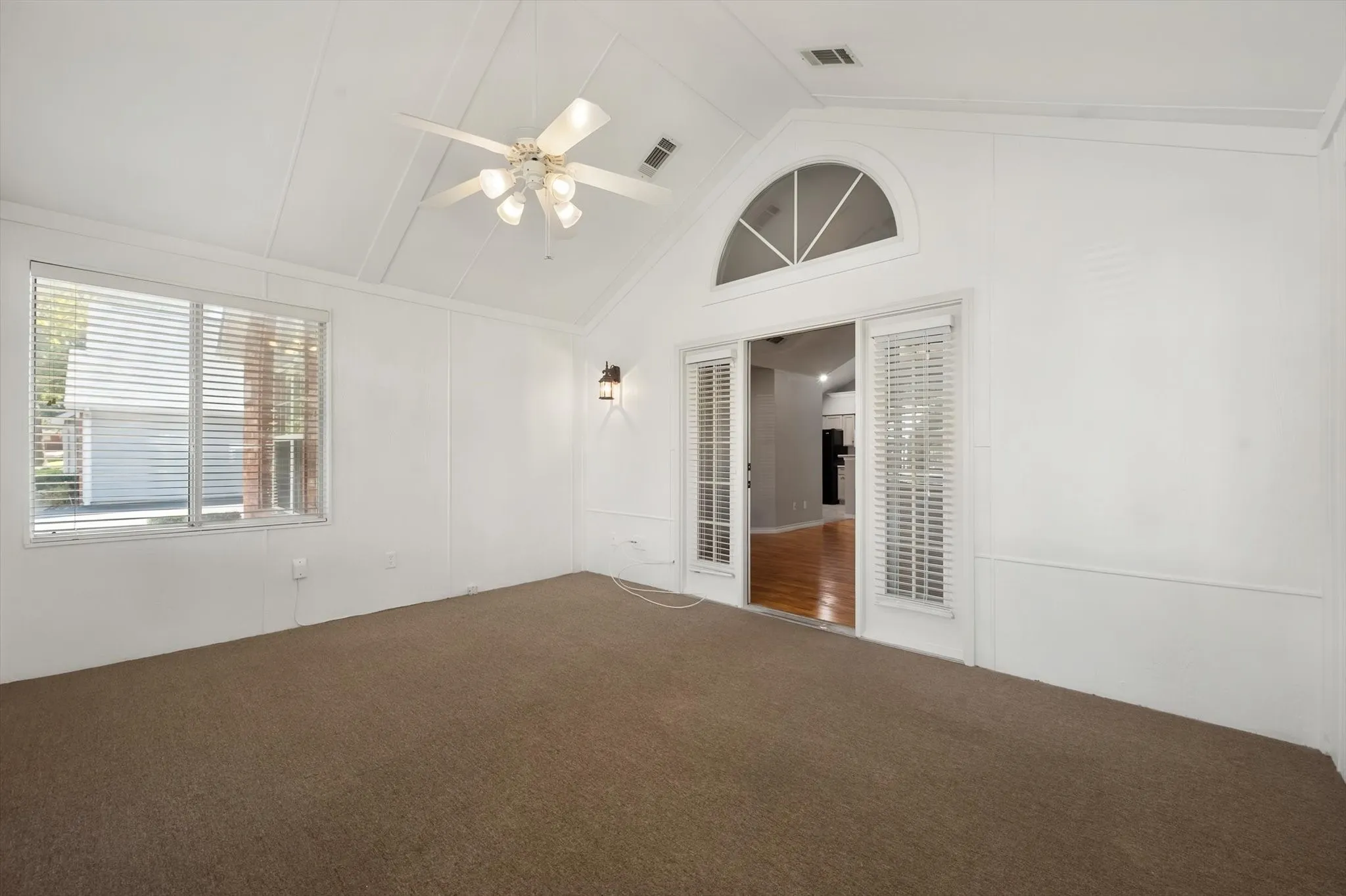 Vaulted ceiling, ceiling fan with light fixture, arched transom window, sliding glass doors, and wall sconces