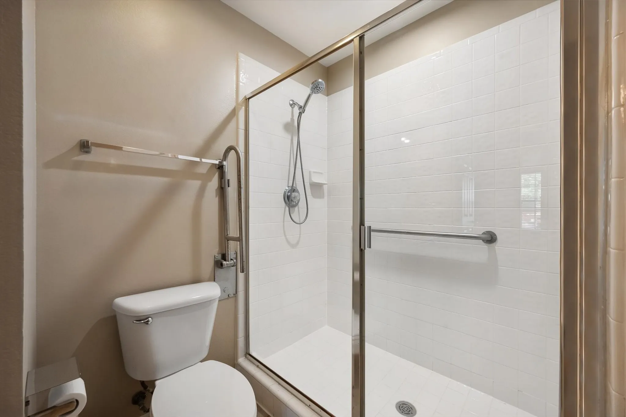 Glass-enclosed shower with white tiled walls, a showerhead, and a grab bar