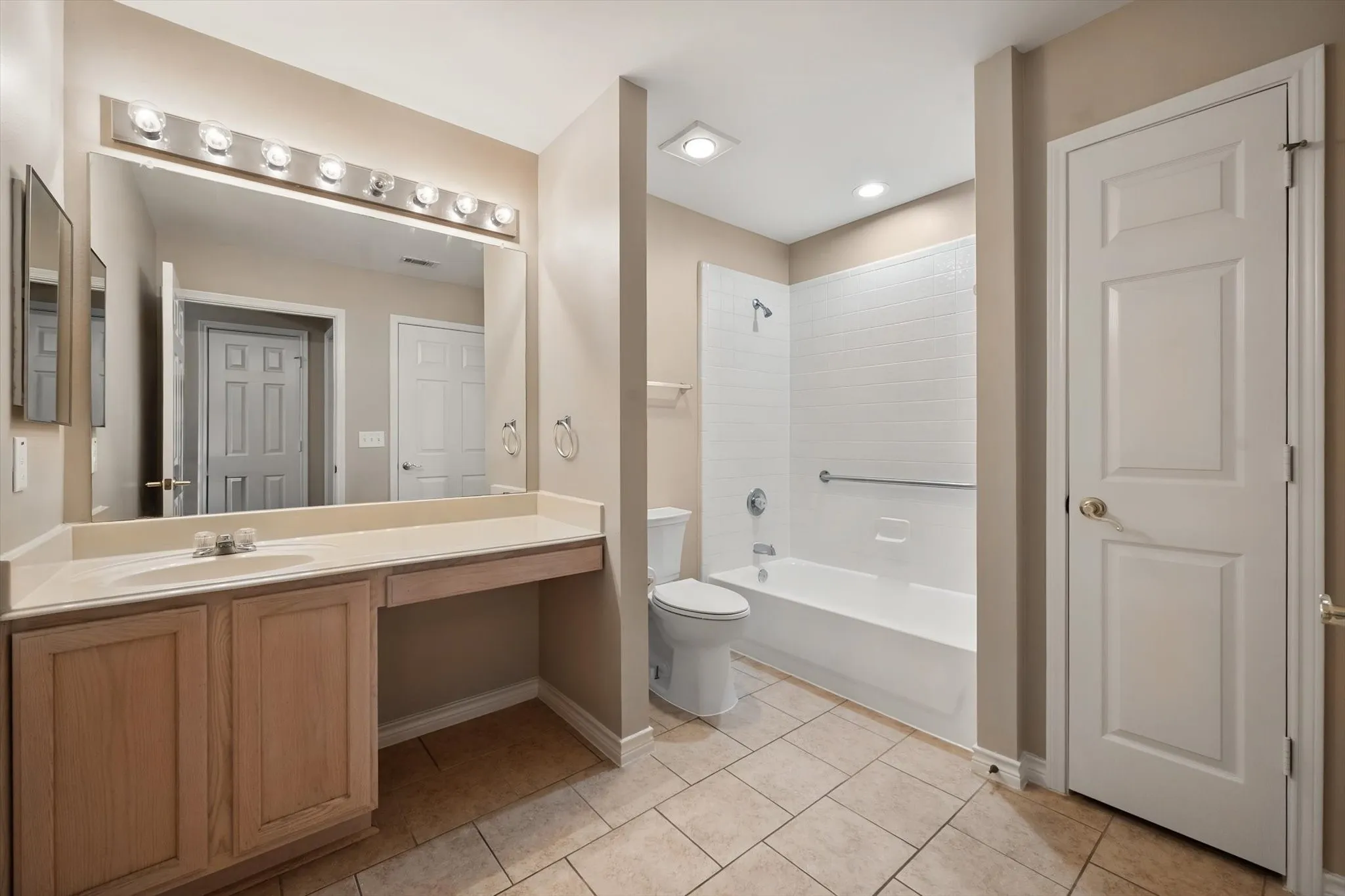 Spacious bathroom featuring a single vanity with extensive counter space, an integrated sink, a full-width mirror, and a combination bathtub and shower with white subway tile surround