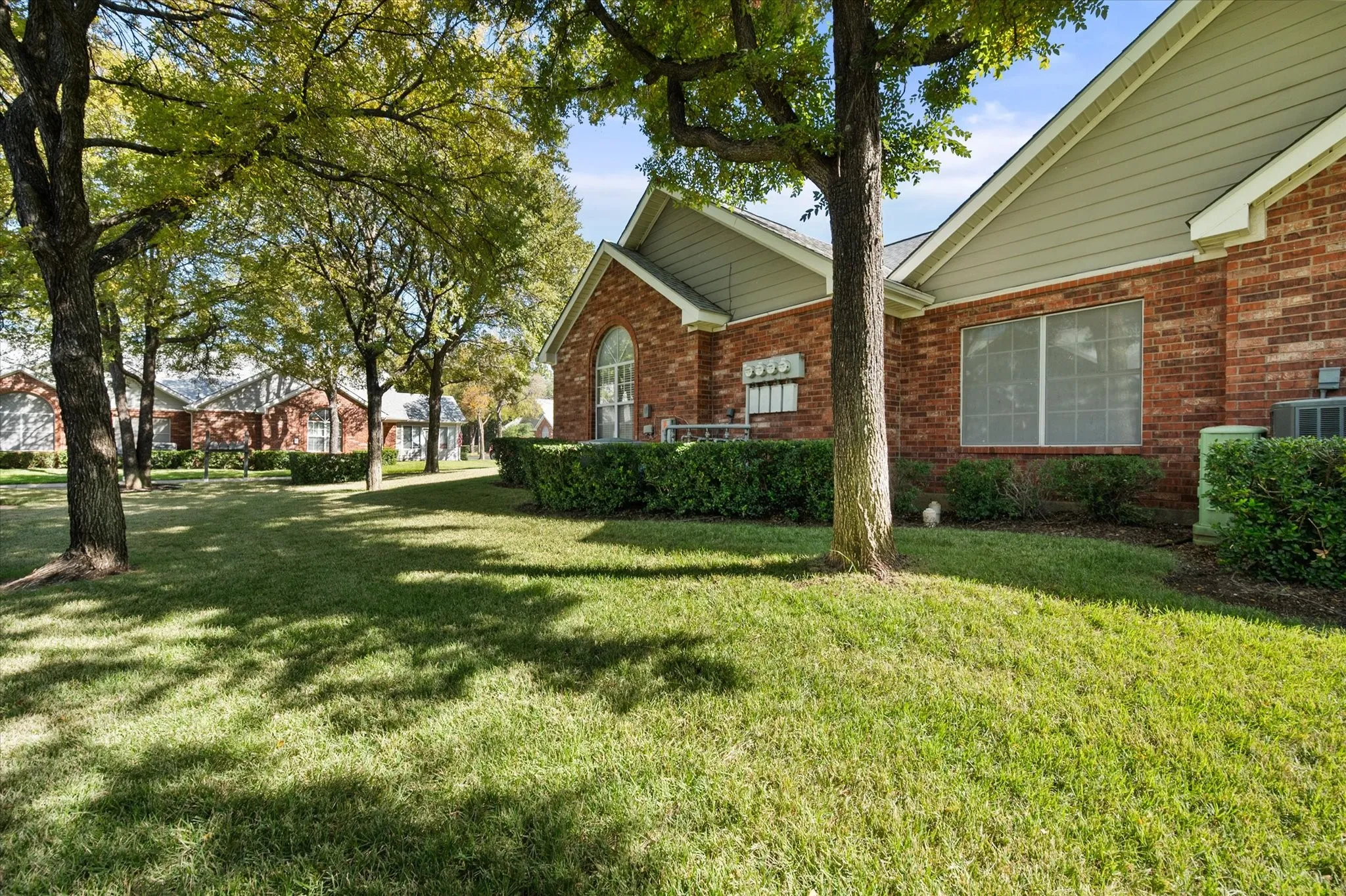 Red brick exterior with arched window, manicured shrubs, and mature trees on a sloped lawn