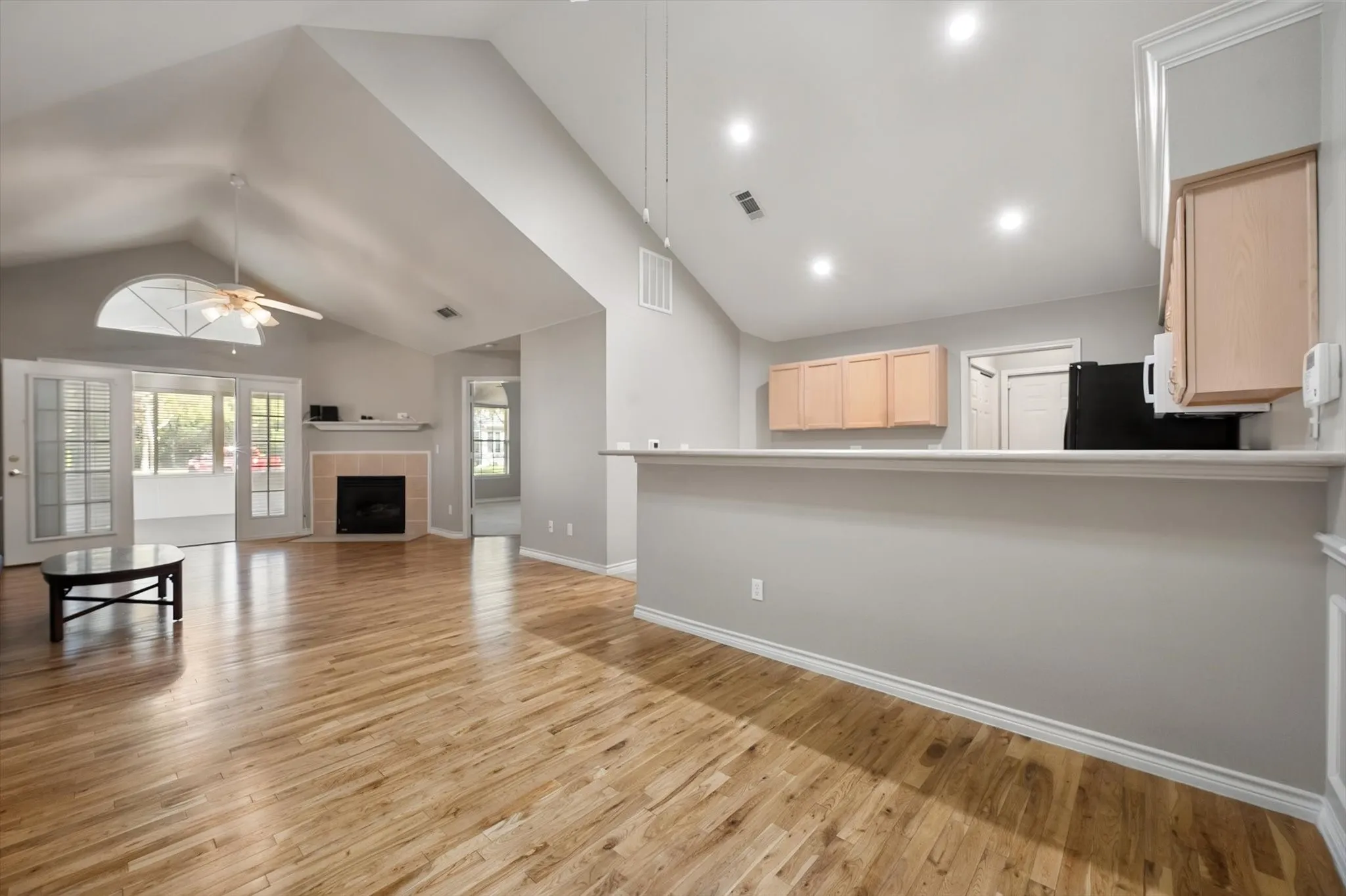 Vaulted ceiling with ceiling fan, wood-finish flooring, fireplace with mantel, French doors, and recessed lighting