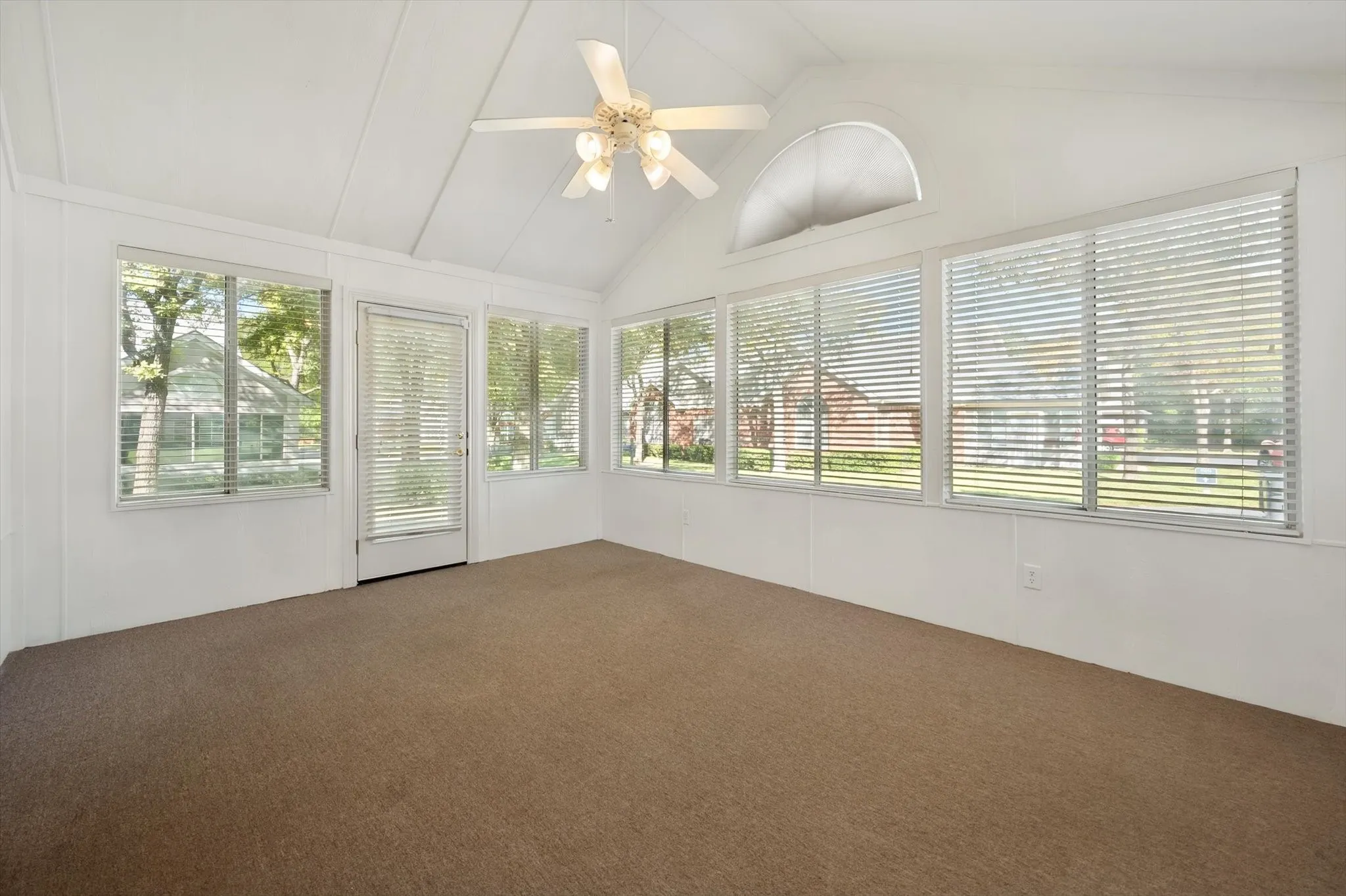 Vaulted ceiling with a ceiling fan, multiple large windows, arched transom window, and carpet flooring