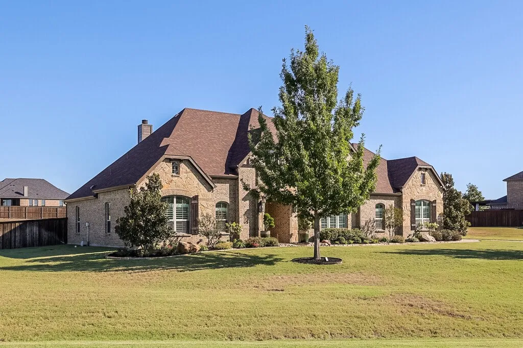 Exterior featuring a brick facade, shingle roof, arched windows, and a manicured lawn