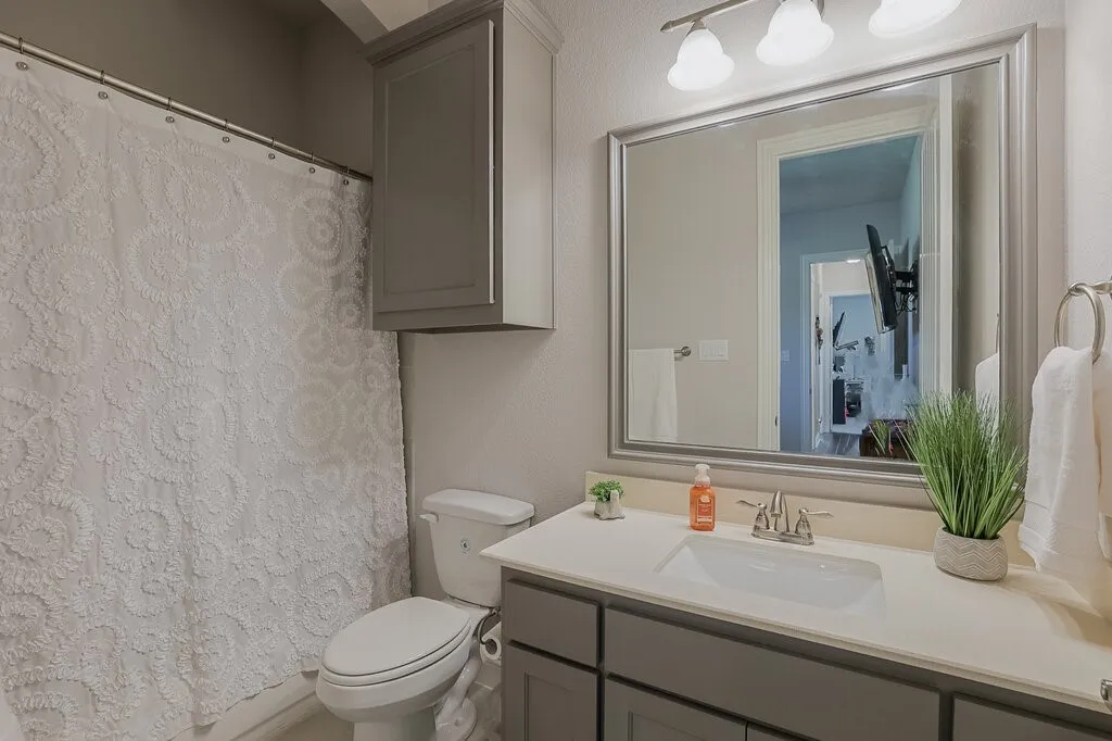 Bathroom featuring a vanity with an integrated sink, framed mirror, wall-mounted light fixture, and overhead cabinetry