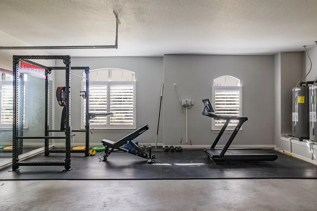Poured concrete flooring, arched windows with plantation shutters, mirrored wall, and wall-mounted water heaters