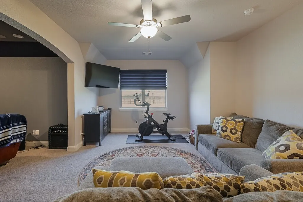 Carpeted living space featuring a ceiling fan with integrated lighting, a wall-mounted television, and a window with blinds