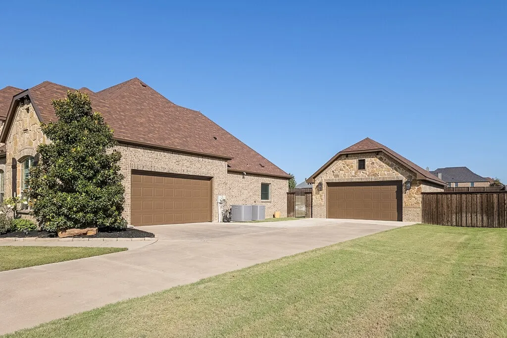Stone and brick exterior with a multi-car garage, separate detached garage, composition shingle roofing, and a concrete driveway