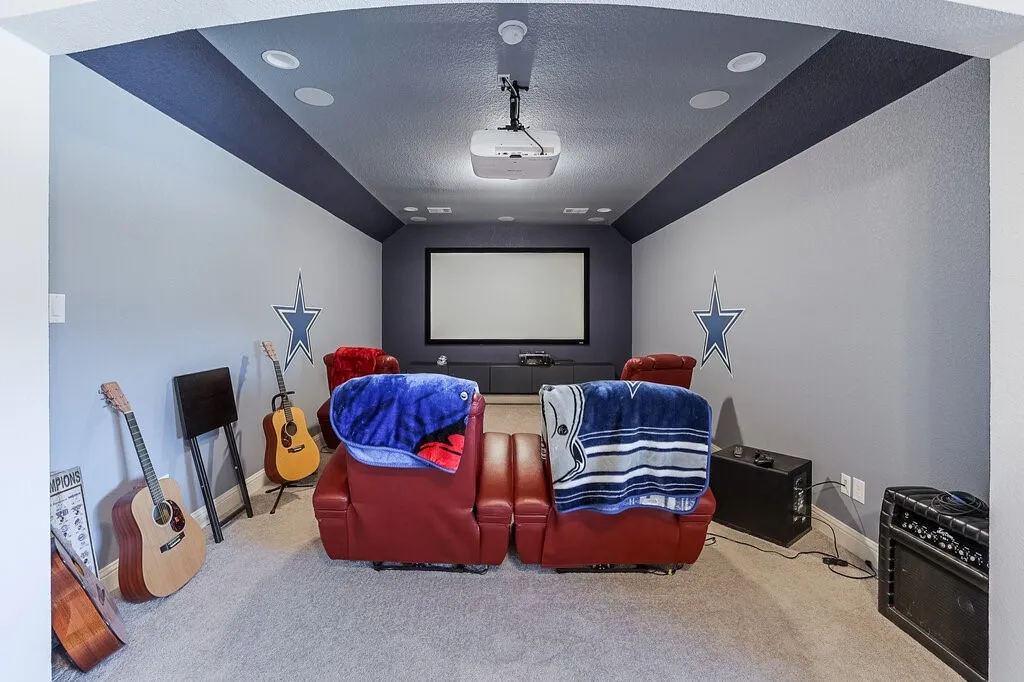 Dedicated media room with projection screen, ceiling-mounted projector, recessed lighting, and sloped ceiling accents