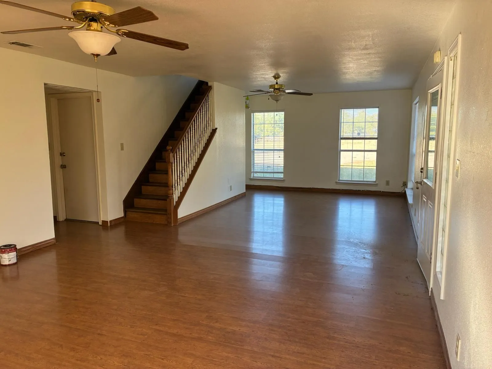 Unfurnished living room with dark wood-style flooring, a ceiling fan, and stairs