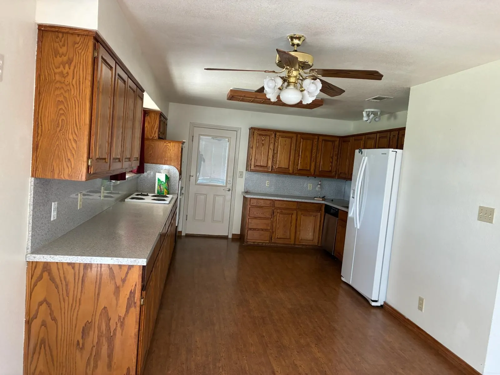 Kitchen featuring brown cabinets, white refrigerator with ice dispenser, light countertops, ceiling fan, and dark wood finished floors