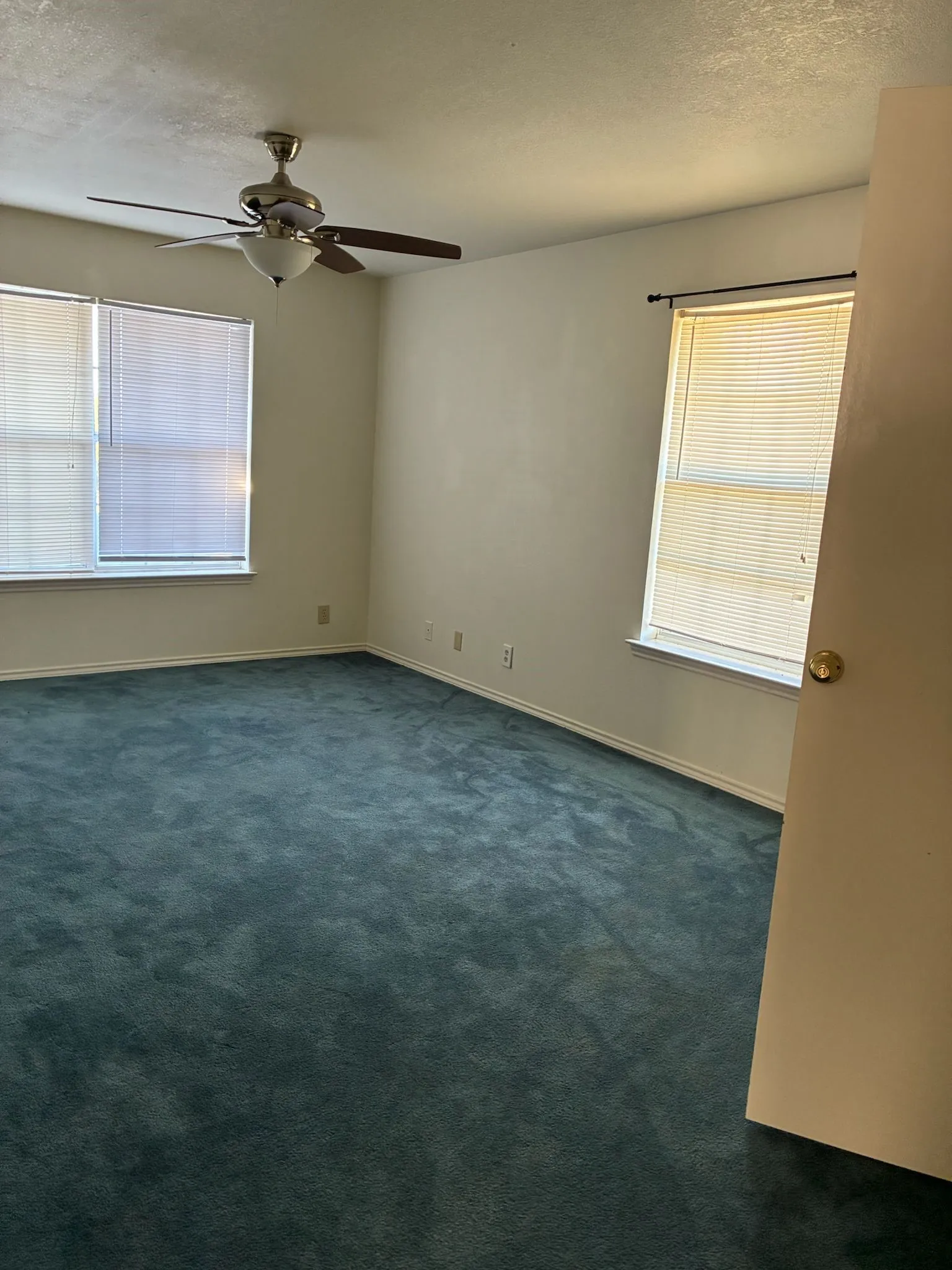 Unfurnished room with a textured ceiling, dark colored carpet, plenty of natural light, and ceiling fan