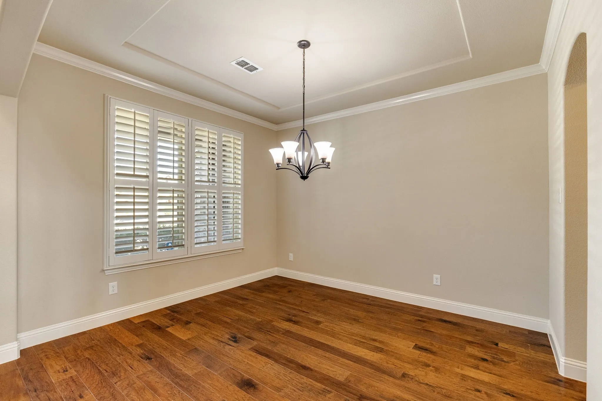 Formal Dining  with Wood-finish flooring, plantation shutters, tray ceiling, and a five-light chandelier