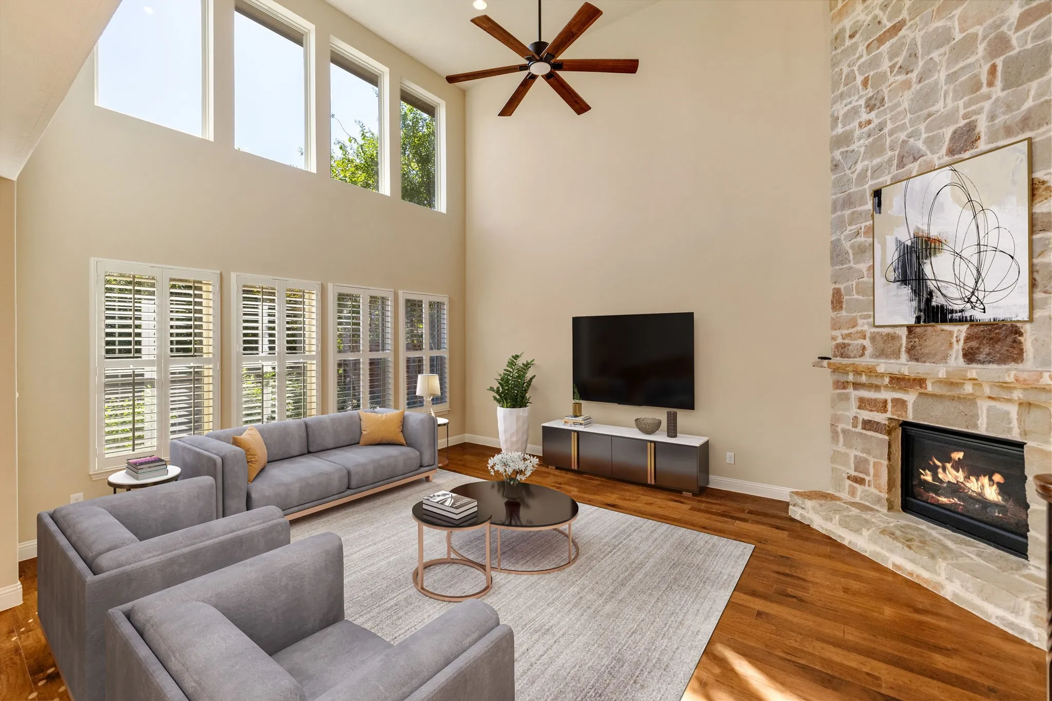 Two-story living area featuring a stone-clad fireplace, elevated windows, wood-finish flooring, and a ceiling fan