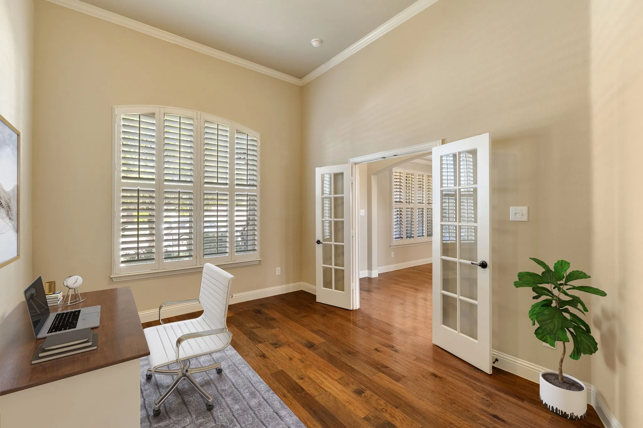 Office featuring hardwood flooring, arched window with plantation shutters, French doors, and vaulted ceiling