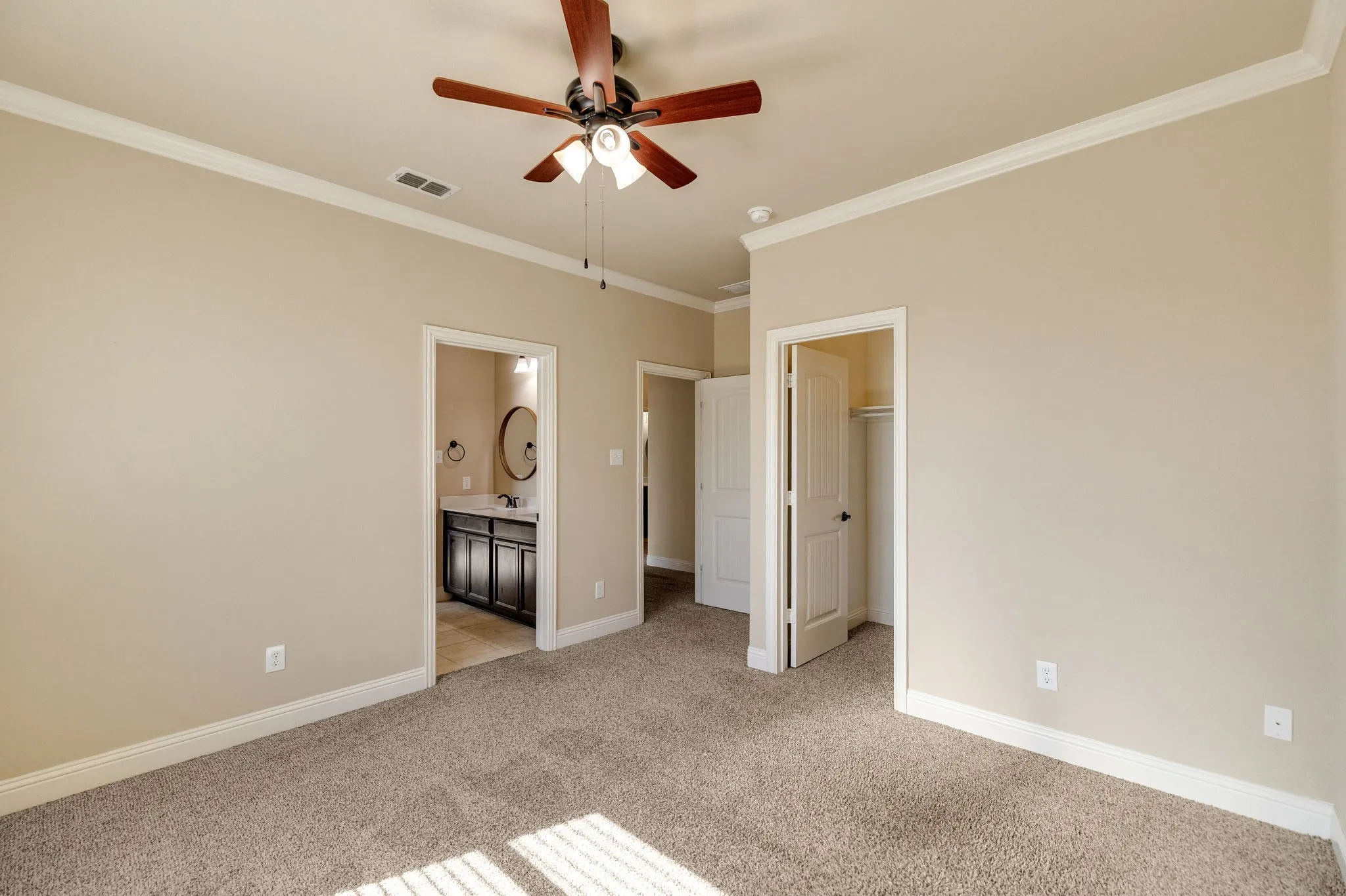 Carpeted room featuring a ceiling fan, crown molding, and an attached bathroom with a dark wood-finish vanity and HUGE walk in closet