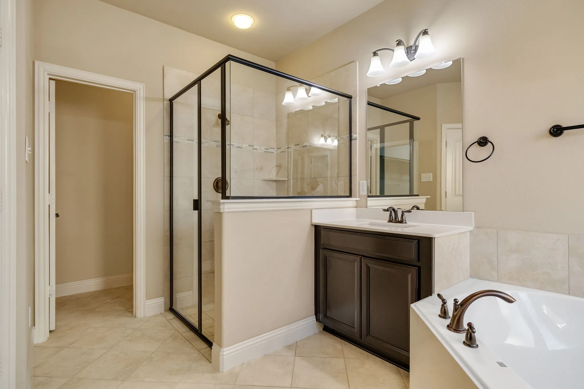 Tiled flooring, dark wood-finish vanity with countertop, frameless mirror, and a walk-in shower with glass enclosure
