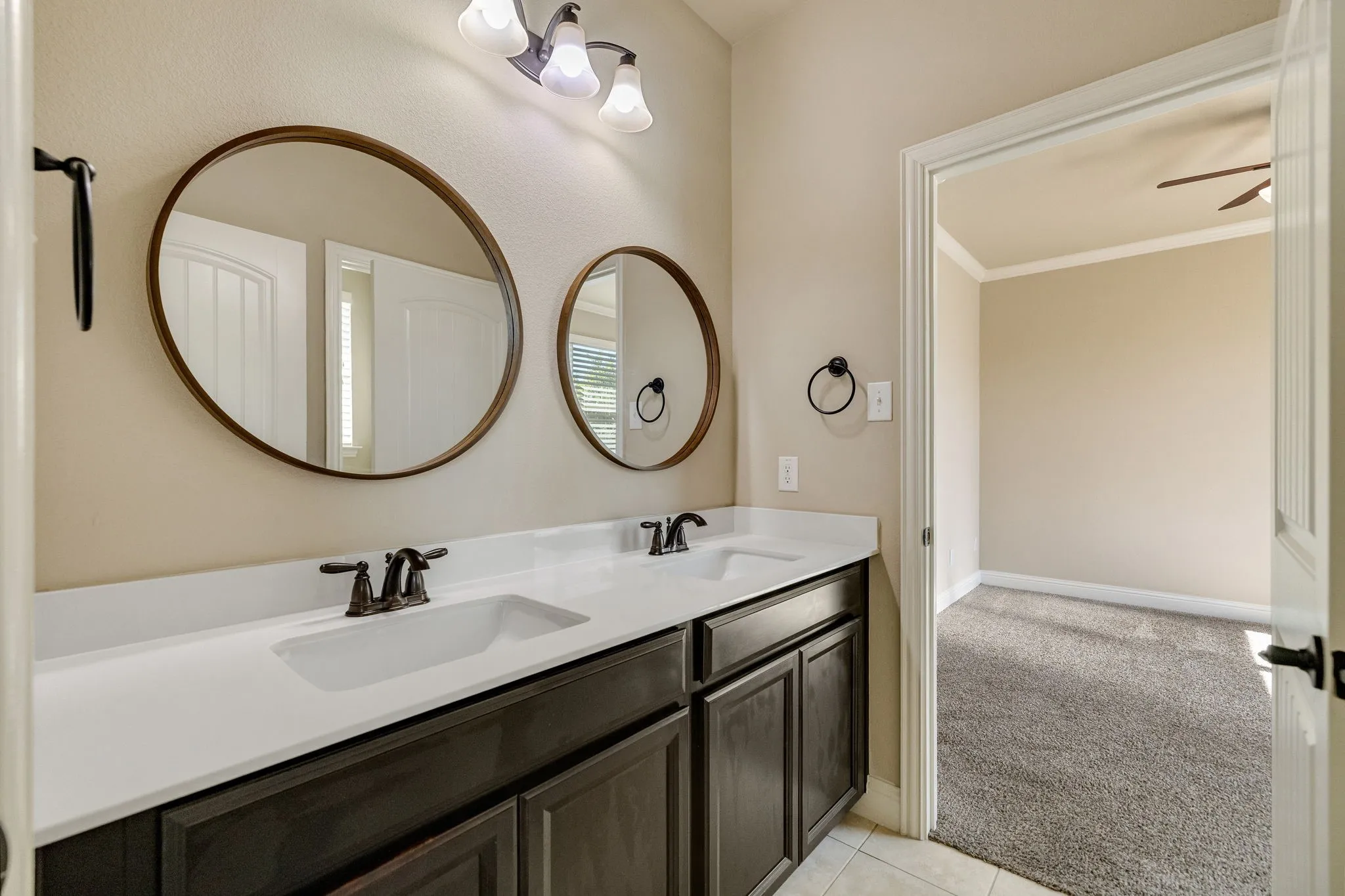 Jack and Jill bathroom featuring dual vanity with dual integrated sinks, dark wood-finish cabinetry, and circular framed mirrors