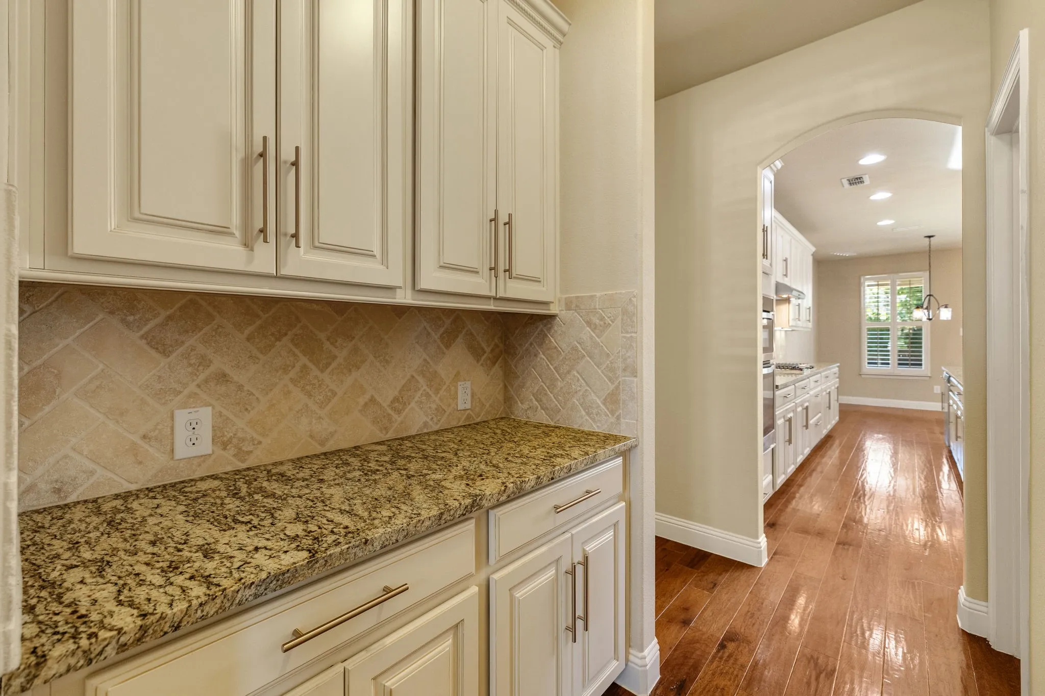 Butlers pantry featuring white cabinetry with brushed nickel pulls, granular countertop, and a herringbone-patterned backsplash