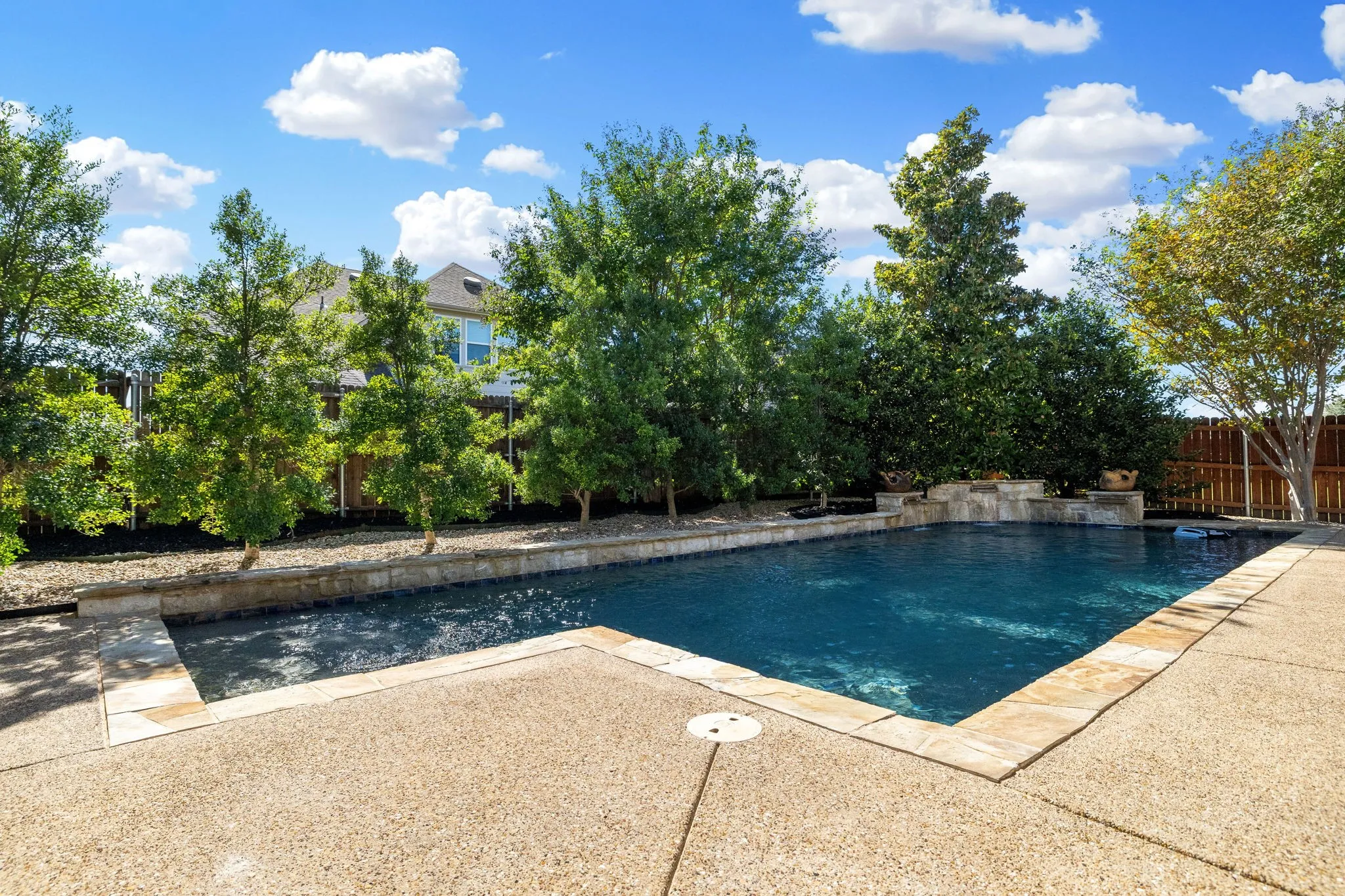 Sparkling in-ground salt water pool with stone coping, surrounded by a textured concrete patio and mature upgraded landscaping